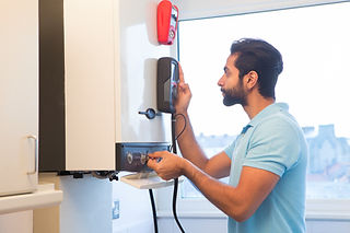 A young male engineer is standing checking the gas central heating boiler in a domestic ho