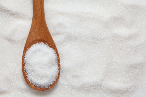 Wooden spoon filled with fine white granulated sugar resting on a bed of sugar crystals