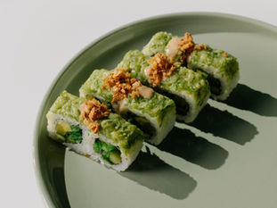 Sushi topped with green wasabi on a green plate.