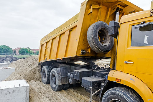 Yellow dumper truck unloading soil or sand at an urban construction site