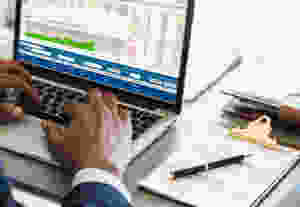 man with a laptop and clipboard looking at financial spreadsheets and invoices