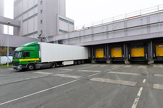 A green and white semi-truck backs into a loading dock at an industrial building