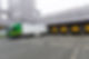 A green and white semi-truck backs into a loading dock at an industrial building