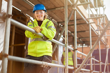a female construction worker stands behind a scaffold and smiles to camera on a building s