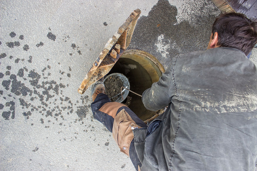 A worker cleans a sewer with a hand bucket