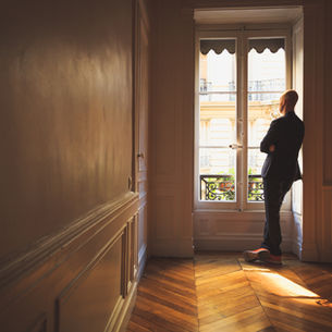 Man wearing a dark suit standing in a quiet space, considering mental health and emotional exhaustion.