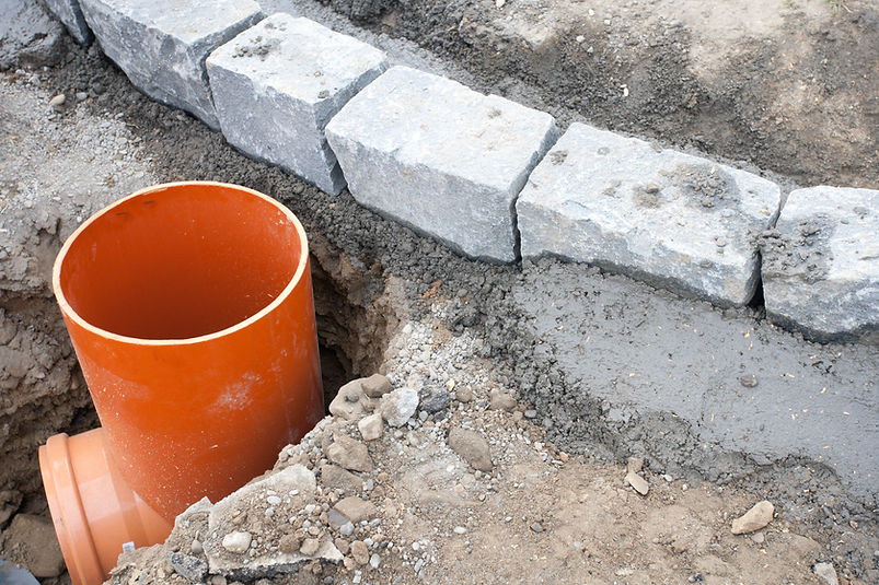 Orange construction pipe is installed in a trench next to a row of grey paving stones