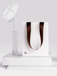 White shopping bag with brown handles and "s." monogram, brand packaging design