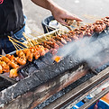 Person grilling skewers of meat over hot coals; culinary background with smoke.