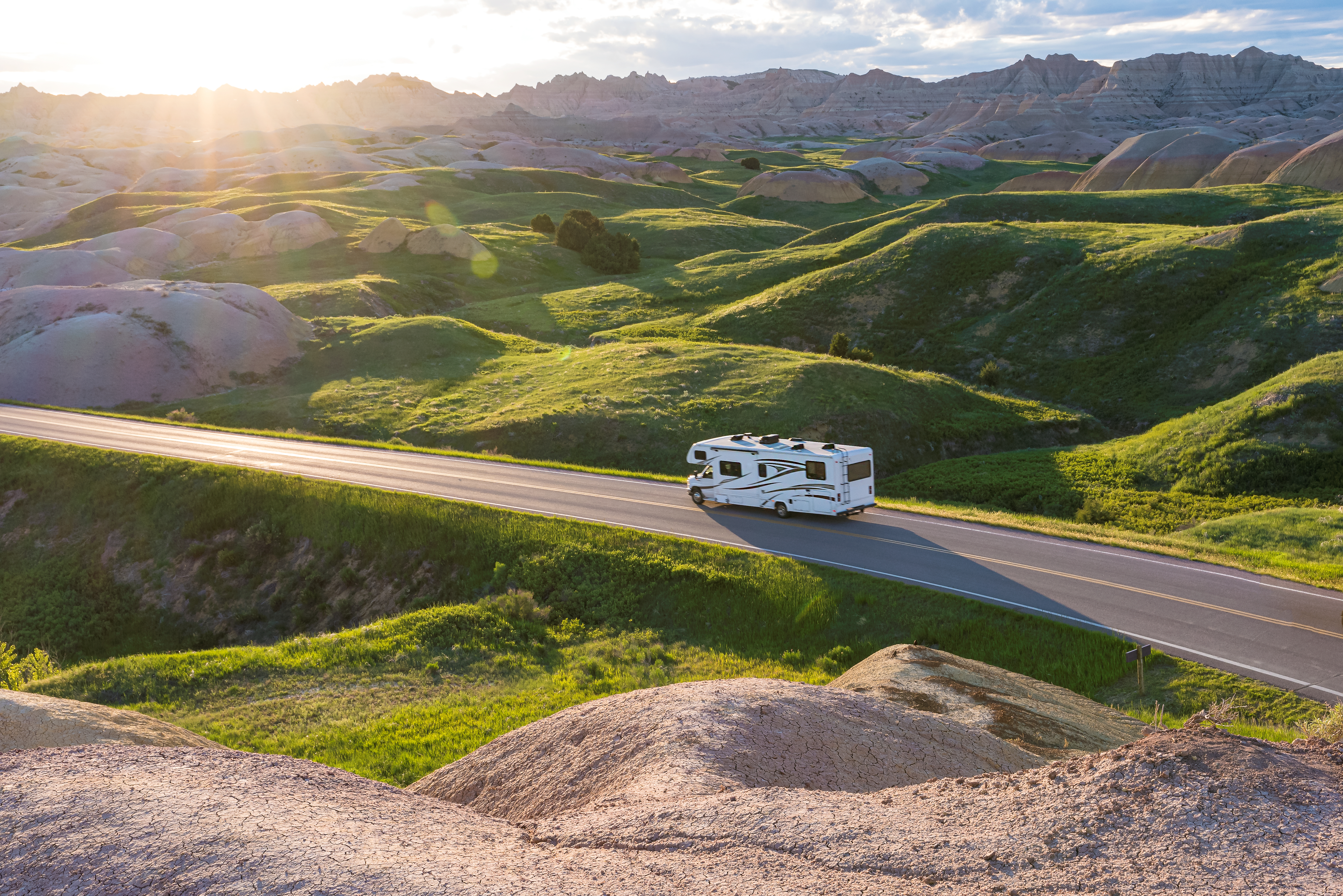This photo shows an RV Driving on a road Through Green Hills