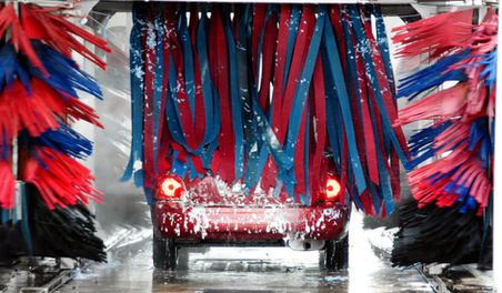 Red car in automatic car wash with red and blue brushes