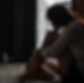 Uma jovem sentada no tapete, de um dos comodos de sua casa muito pensativa. Aparenta estar triste.