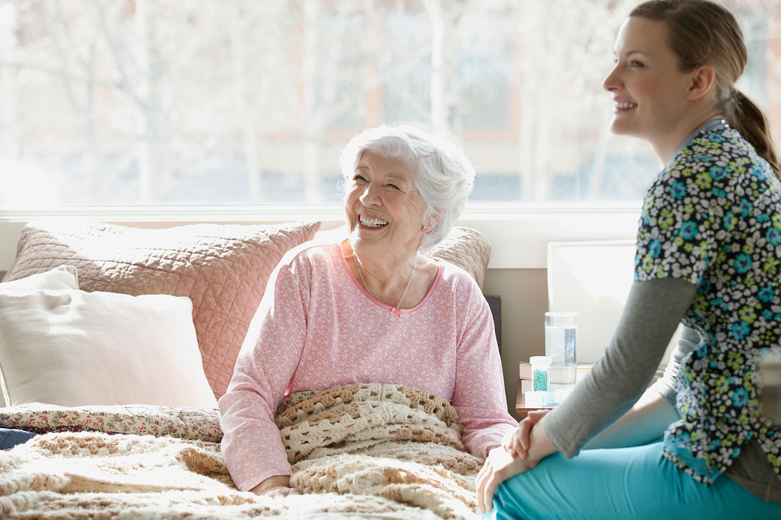 A smiling elderly woman looking up cheerfully at her carer in a brightly lit room indoors