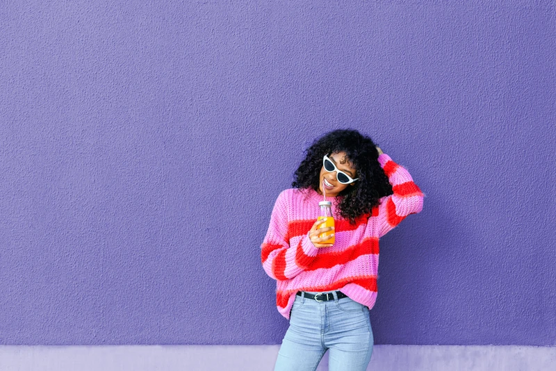 a woman in a pink and red striped sweater is holding a bottle of orange juice