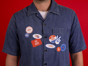 Man with a denim button down shirt with lots of I voted type stickers.