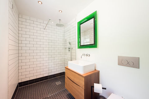 A walk in shower wetroom with glass screen, white tiles and green mirror in a bathroom wit