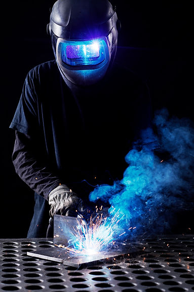 A welder in a dark setting uses a welding torch