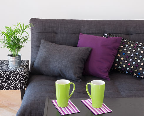 Sofa decorated with bright cushions, green plant and big cups on a table