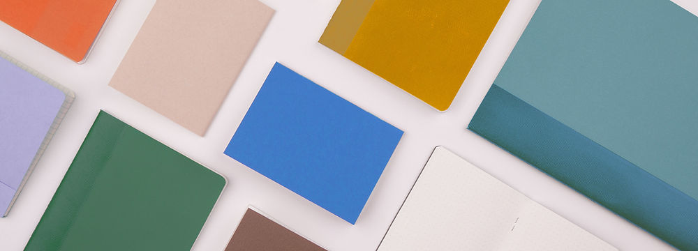 Various colorful notebooks arranged on a white surface, open and closed, flat lay.