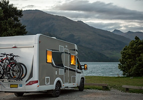 A motorhome parked by a serene lake against a backdrop of mountains at dusk.