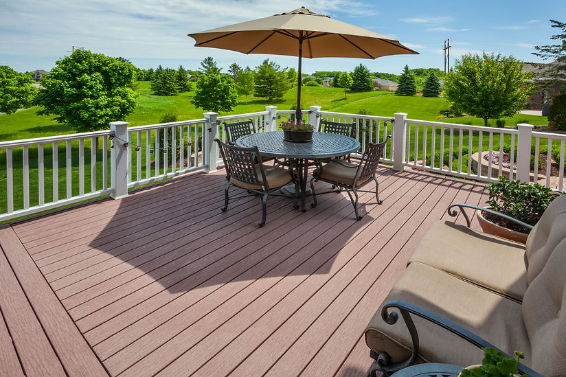 Elevated wooden deck with a patio table, chairs, parasol, and white railings overlooking green countryside