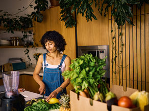 A woman cuts vegetables in her kitchen full of plants.