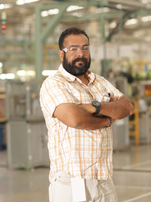 Bearded man with glasses standing arms crossed confidently in a factory.