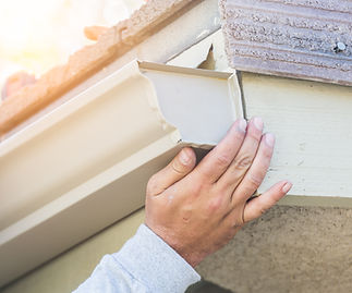 A person's hand fitting a cream gutter end cap onto the edge of a roof