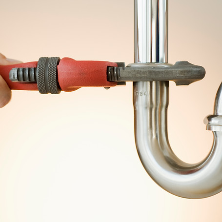 A hand uses a large red wrench to tighten a chrome pipe under a sink