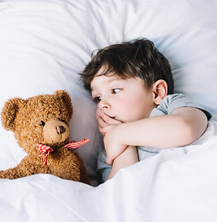 Toddler laying down with Teddy Bear on bed