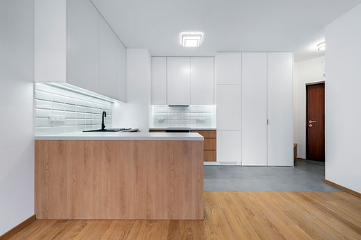 Minimalist white kitchen design with handleless cabinetry, a light wood counter, and tile backsplash