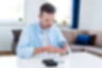 Man in a light blue shirt checking blood sugar levels with a glucose meter at home.