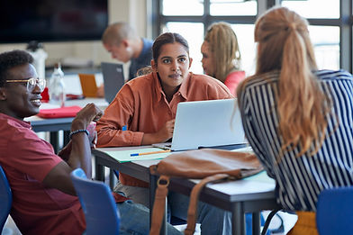Young man and woman looking at female university student while discussing in classroom
