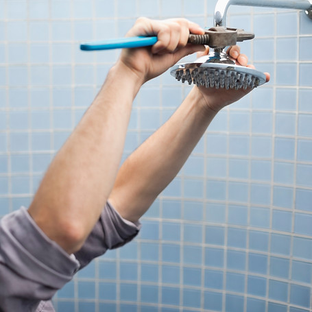 A person's hands are using a blue-handled wrench to install a shower