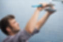 A man in a gray shirt uses a wrench to adjust a showerhead in a tiled bathroom.