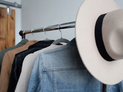 Porte-vêtements avec plusieurs vestes et un chapeau beige, posé devant un mur en bois.