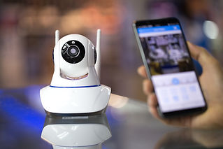 A white security camera on a glass table with a smartphone, suggesting remote monitoring