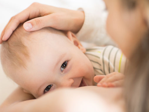 Smiling baby cuddled close as an adult’s hand strokes their head in a soft, warm close-up.
