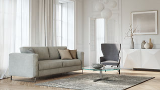 Bright Scandinavian living room with light grey sofa, dark grey armchair, round glass coffee table, and chevron wood floor.