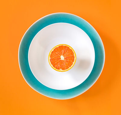 Half an orange sits on a white plate with a blue surround. The background is bright orange