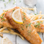 Tender battered fish filets sprinkled with parsley and garnished with lemon slices and a side of tartar sauce.