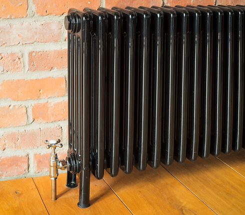 Black cast iron old style radiator against a brick wall on a wooden floor