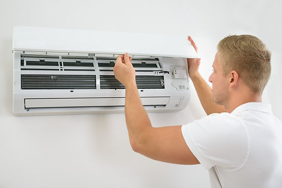 A technician lifts open the front panel of a white indoor wall-mounted air conditioning unit to service or check the internal components