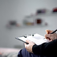 Individual seated on a bed, focused on writing with a pen and paper in hand
