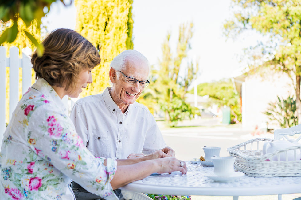 Smiling senior man in glasses chatting with a woman outdoors over tea on a sunny patio