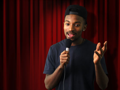 Man on stage with a microphone gesturing to the audience