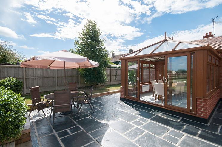 Timber frame conservatory with sliding glass doors opening onto a patio garden with outdoor seating