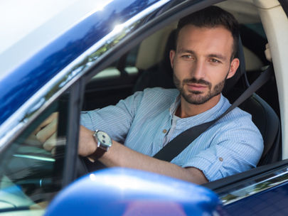 A man looking out the window while driving a blue car