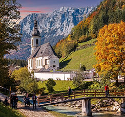 A traditional old house surrounded by green hills and countryside landscape in Bavaria, with rolling terrain in the background.