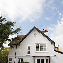 A white two-story house with a triangular roof, surrounded by tall green